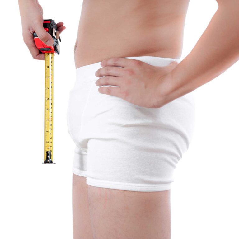 Mann in Boxershorts misst Penisumfang mit Maßband – symbolische Darstellung für das Thema Penisvergrößerung.